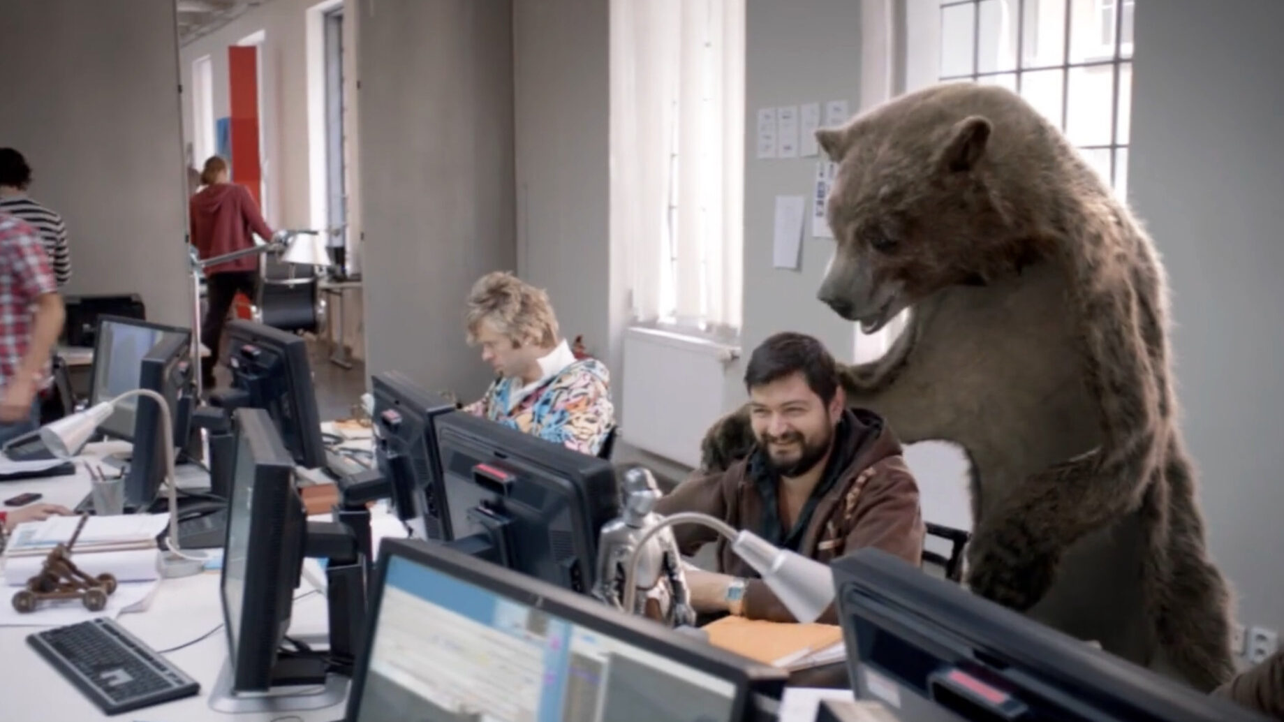 canal + 'the bear', a bearskin rug film director has his arm around a video editor in an office.