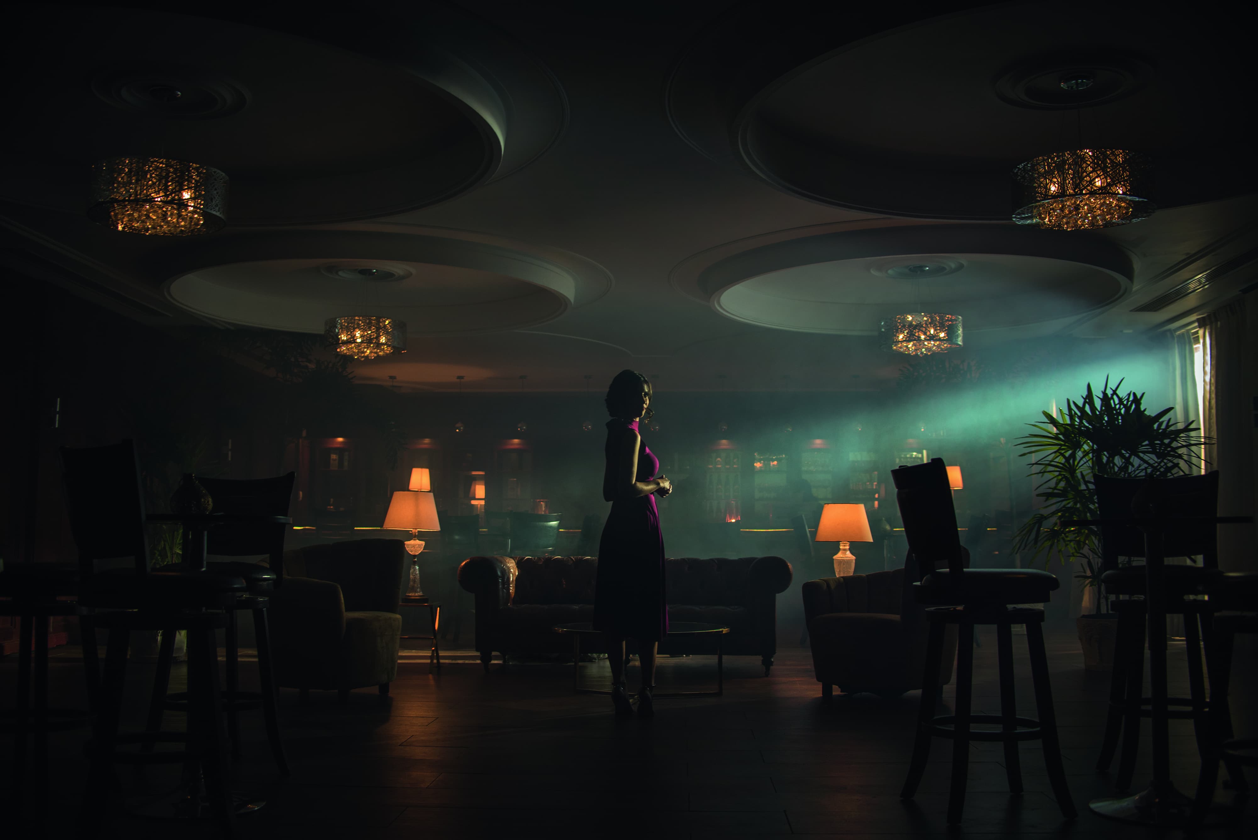 A woman stands in a grand. dimly lit empty bar