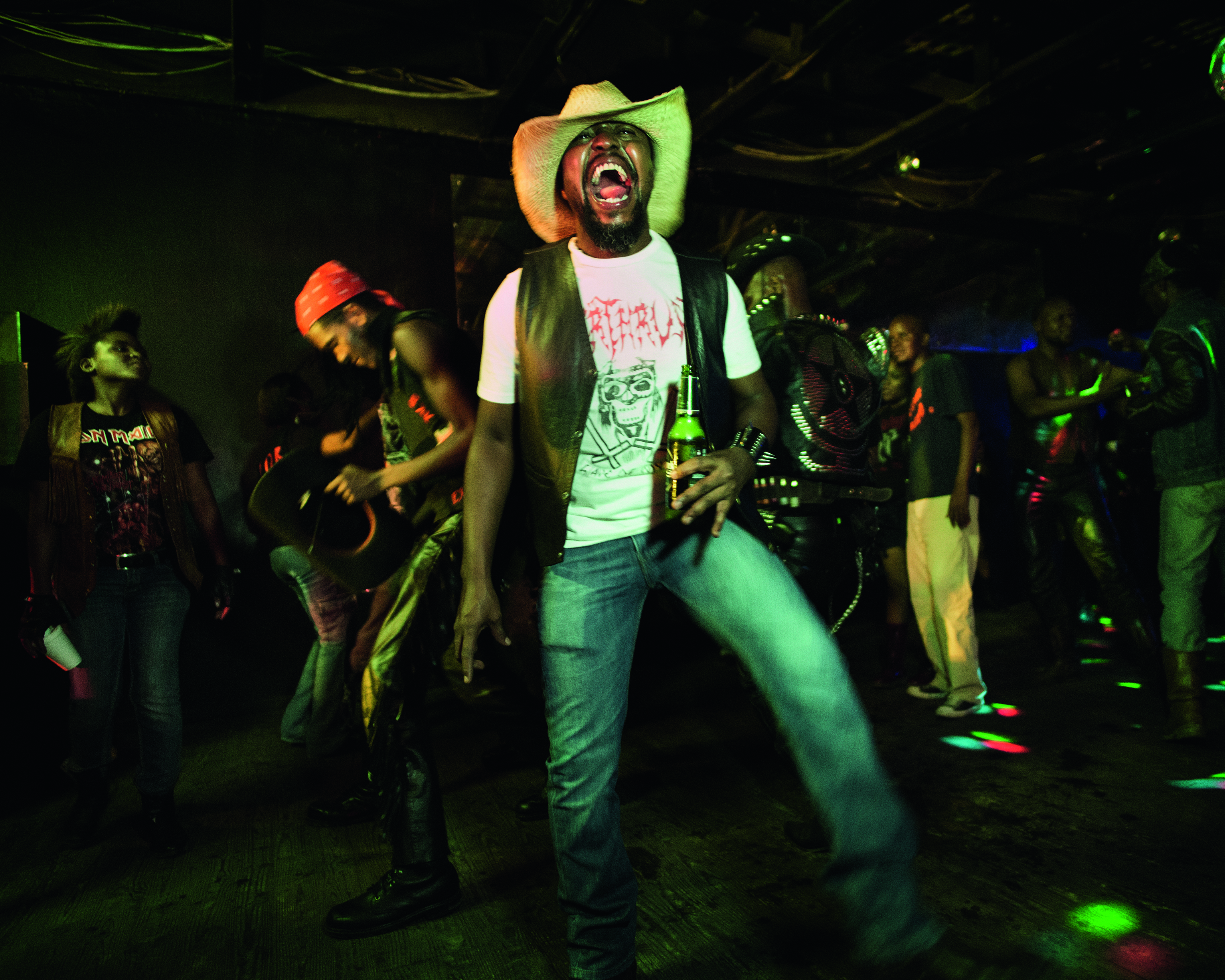 The Hellbangers of Botswana, a man in a club faces the camera, holding a bottle of beer